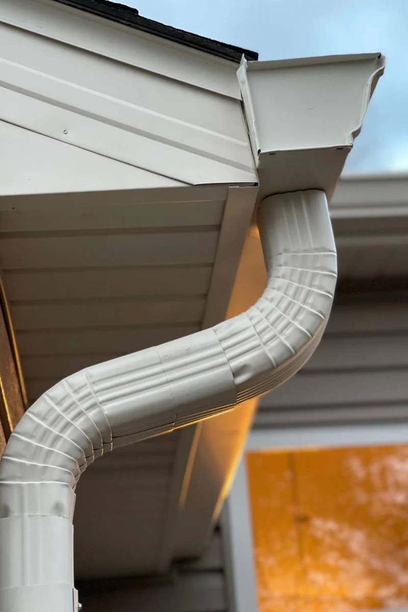 White gutter outlet and downspout beside soffit and fascia